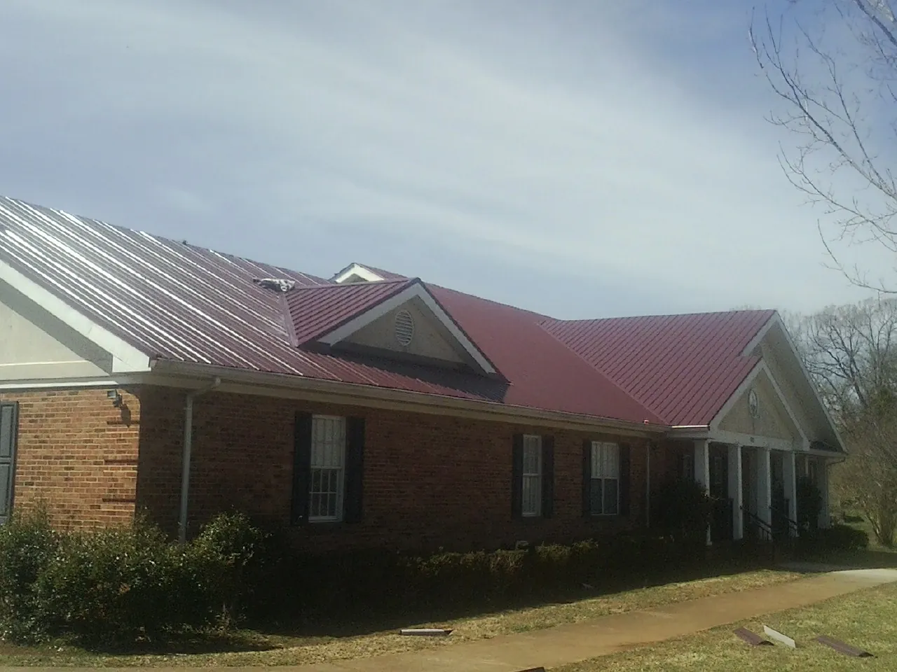 Red metal roof with gabled entries on a long brick building, from a Hail Damage Roof Repair job in Corning