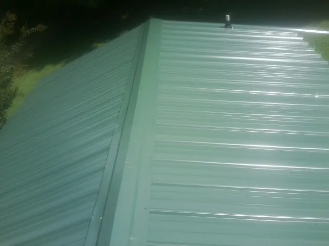 New green metal panels meeting at the ridge of a roof — Flat Roof Repair work by our crew in Corning