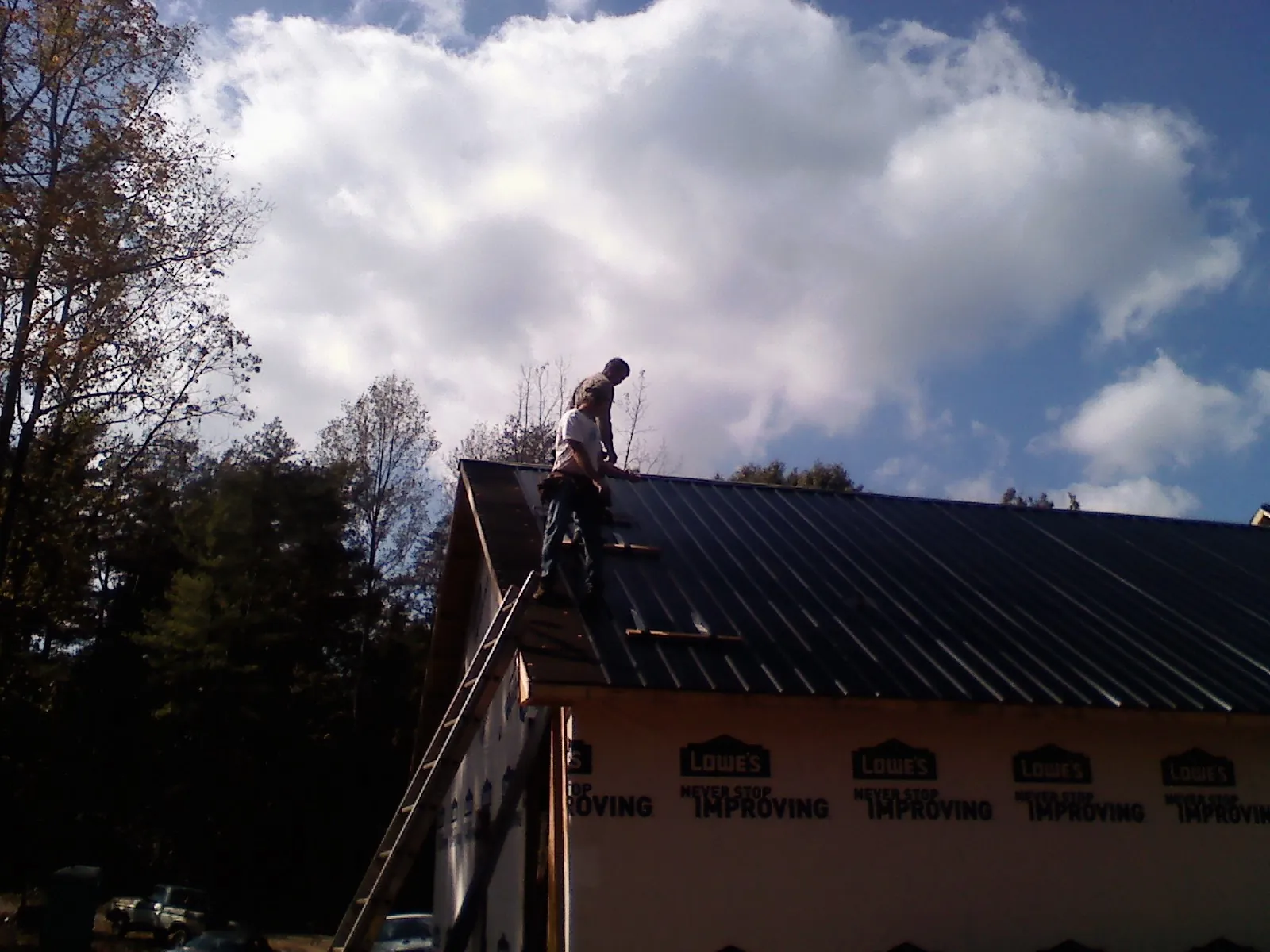 Roofer fastening dark metal panels high against a cloudy sky, from a Roof Inspection job in Corning